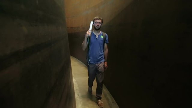 Visitor walking down curved narrow passage between walls, listening audio guide