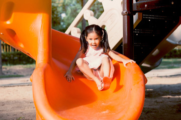 Cute asian child girl having fun to play slider in the playground in summer time