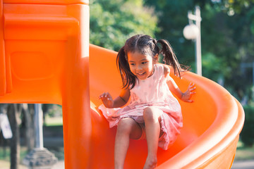 Cute asian child girl having fun to play slider in the playground in summer time