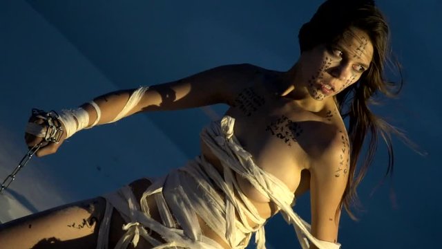 A woman mummy in the rays of light sits on dand in desert and holds a chain in her hand