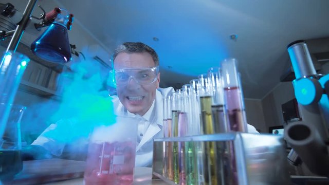 Man in medical gown and glasses watching chemical reaction in test tube.