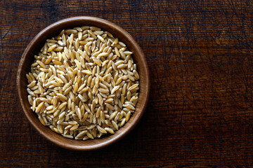 Kamut wheat kernels in dark wooden bowl isolated on dark brown wood from above.