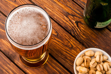 galss of cold frothy lager beer, nuts, bottle, old wooden table