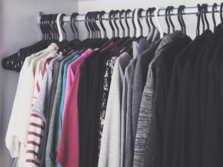 Obraz premium Woman's color-coordinated closet full of fashionable trendy clothes like t-shirts, blouses, sweaters, blazers, shirts and jackets. 