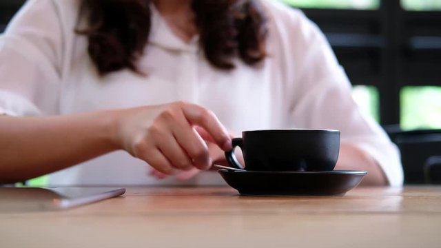 A woman receiving a black coffee cup from waiter and drinking it in coffee shop