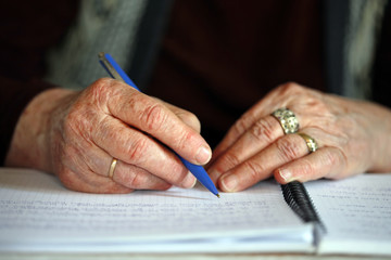 Close up of elderly woman's hands with pen; old woman is writing; life-long learning concept; selective focus background.