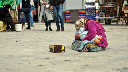 Shamed homeless woman with child in her hands is begging for the money on the street; people and...
