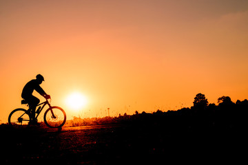 Fototapeta premium A man rides a bicycle in the evening with orange sky,Silhouette sporty image concept.