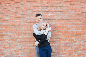 Obraz na płótnie Canvas Happy young couple hugging and smiling on a background of red brick wall. Blonde girl with blue eyes and a young man of Arab appearance with brown eyes