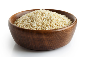 Decorticated sesame seeds in dark wooden bowl isolated on white.