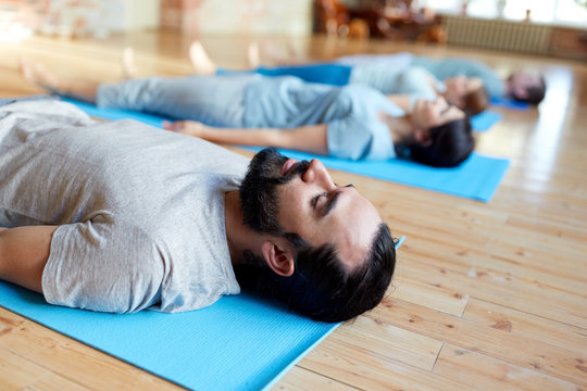 man with group of people doing yoga at studio