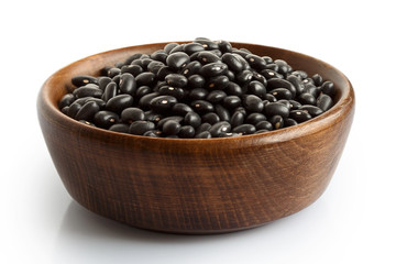 Dry black beans in dark wooden bowl isolated on white.