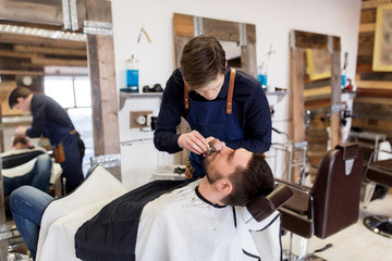 man and barber with trimmer cutting beard at salon