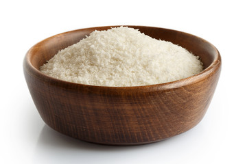 Desiccated coconut in dark wooden bowl isolated on white.