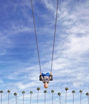 Boy swinging upside down on a swing over a row of palm trees, Orange County, California, America, USA