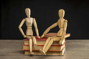 Close up shot of male and female wooden mannequins sitting on books education concept
