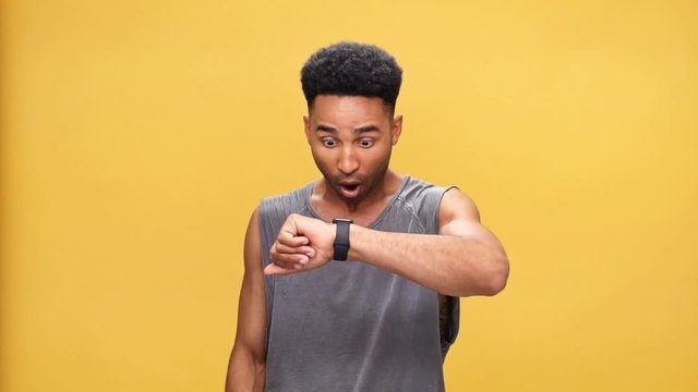 Young handsome african man looking at watch over yellow background