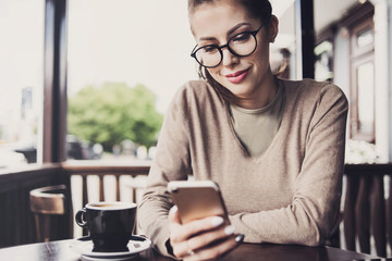 Image of woman using smartphone in cafe. Young beautiful girl sitting in a coffee shop and texting her mobile phone