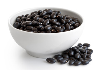 Black beans in white ceranic bowl isolated on white. Spilled seeds.
