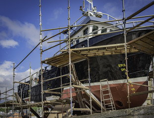Fishing trawler in dry dock for maintenance and painting with scaffolding and tools in view