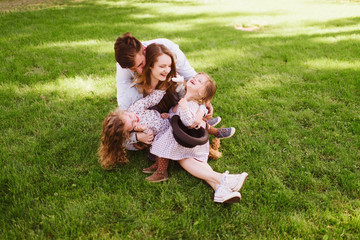 Young cheerful family sitting on grass enjoying vocation and playing with their children. People having fun in summer park. Sunny day. Outdoor