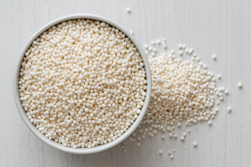 Dry tapioca pearls in white ceramic dish isolated on painted white wood from above. Spilled tapioca.