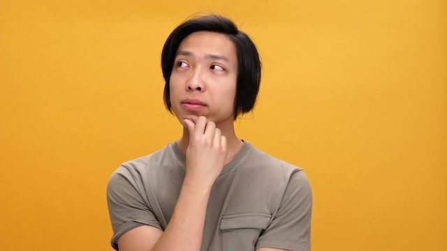 Young asian thoughtful man and looking aside isolated over yellow background