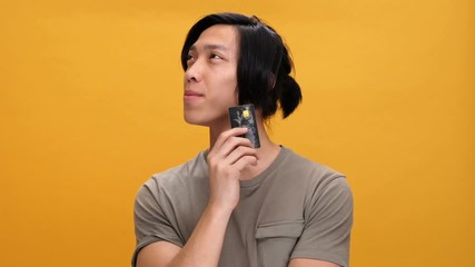 Young asian man smiling holding credit card thinking isolated over yellow background