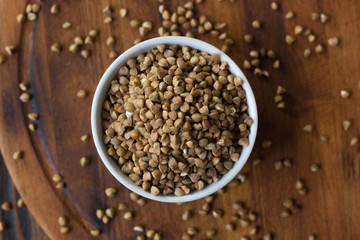 Buckwheat grain on ceramic bowl over wooden table.