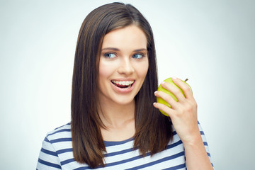 Close up smiling face portrait of young woman with braces on teeth holding green apple.