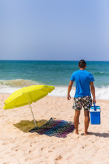 Young man with ice bar cooler under solar umbrella on a beach near ocean