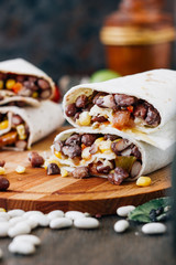 Nice vegetarian burrito over black table on wooden board.