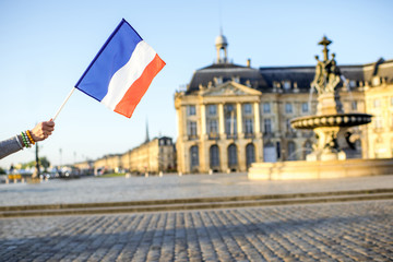Fototapeta na wymiar Holding a french flag on the famous central square background in Bordeaux city