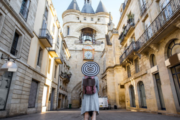 Young woman tourist with big hat standing back in front of the famous bell tower in Bordeaux city...