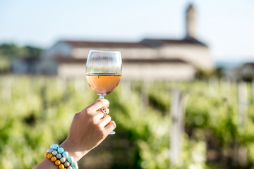Woman holding a glass with rose wine on the vineyard background during the sunset