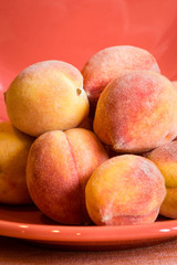 Close up of fuzzy whole peaches on an orange plate.