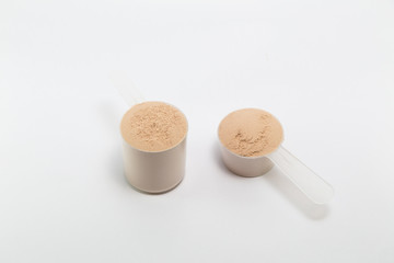 heap of isolate and chocolate protein powder with plastic spoon on white background