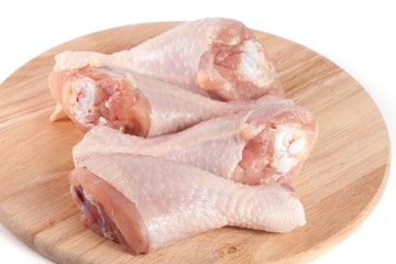four raw chicken drumsticks on a wooden cutting boardn white background