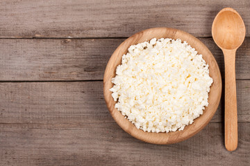 Cottage cheese in a wooden bowl on old wooden background with copy space for your text. Top view