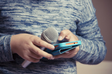 Girl holds a microphone in her hand and looks for a song in the phone for karaoke performance.