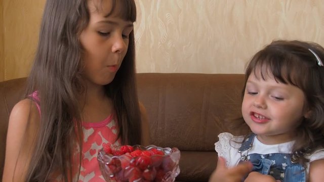 A child eats raspberries. Two sisters feed each other raspberries.