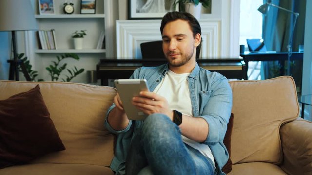 Attractive young man using tablet while relaxing on the sofa at the living room.