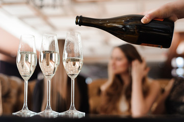 Fototapeta na wymiar Man fills glasses of champagne for three beautiful young women in restaurant