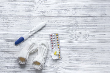 Pregnancy planning. Contraceptive pills, pregnancy test and booties on wooden background top view copyspace