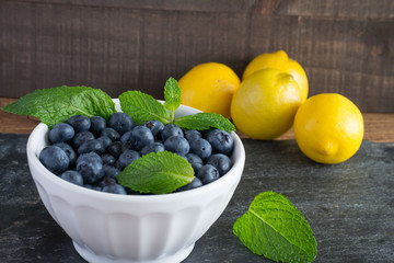 Blueberry fresh from the garden with mint leaves and tart sweet yellow lemons in a rustic background