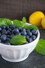 Fresh, Sweet blueberries in a stylish white bowl with mint herb leaf and lemon in the background