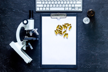 Workplace in laboratory. Microscope, pad and pills on grey stone background top view mockup