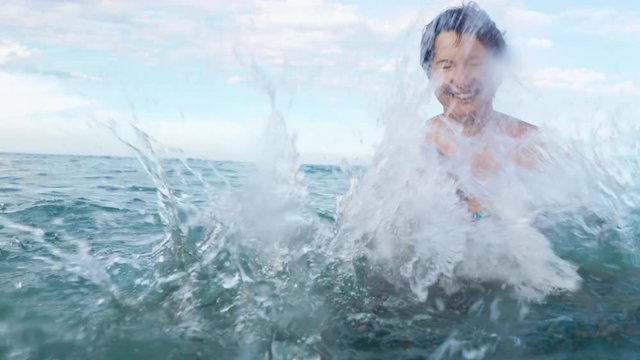 happy boy makes splash in the sea slow motion. boy in swimming goggles and his mother having fun in the sea