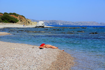 Naga kobieta z zakrytą twarzą opala się na skraju morza.