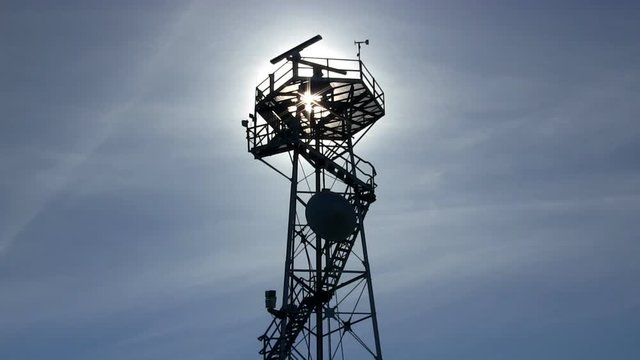Marine traffic control radar tower silhouette with spinning antenna against blue sky and wispy clouds